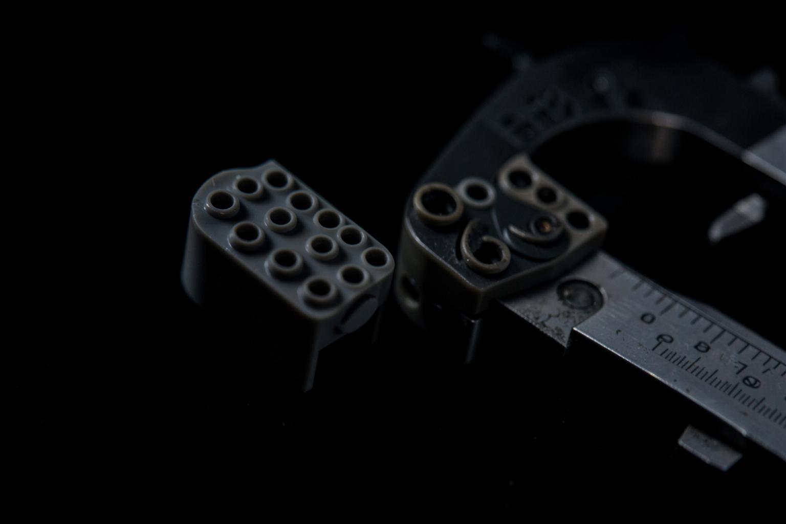 Macro close-up of a plastic building brick measured with a caliper to check stud tolerance