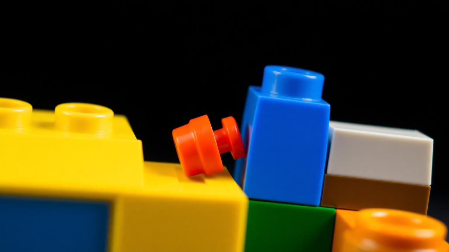 Macro close-up comparing a small 4.8mm LEGO stud with a larger 9.6mm Duplo anti-stud on colorful ABS bricks